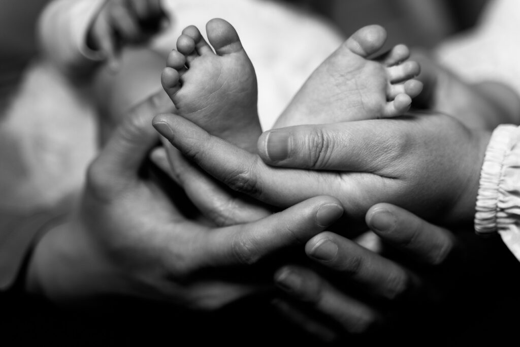 Newborn portrait of baby's feet with mom and dad embracing her.