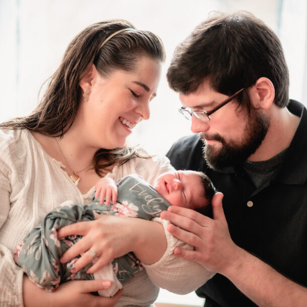 New parents gaze lovingly at their newborn baby daughter at home with natural light.