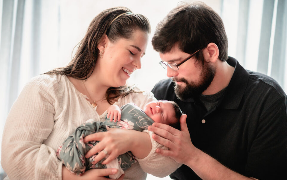 New parents gaze lovingly at their newborn baby daughter at home with natural light.