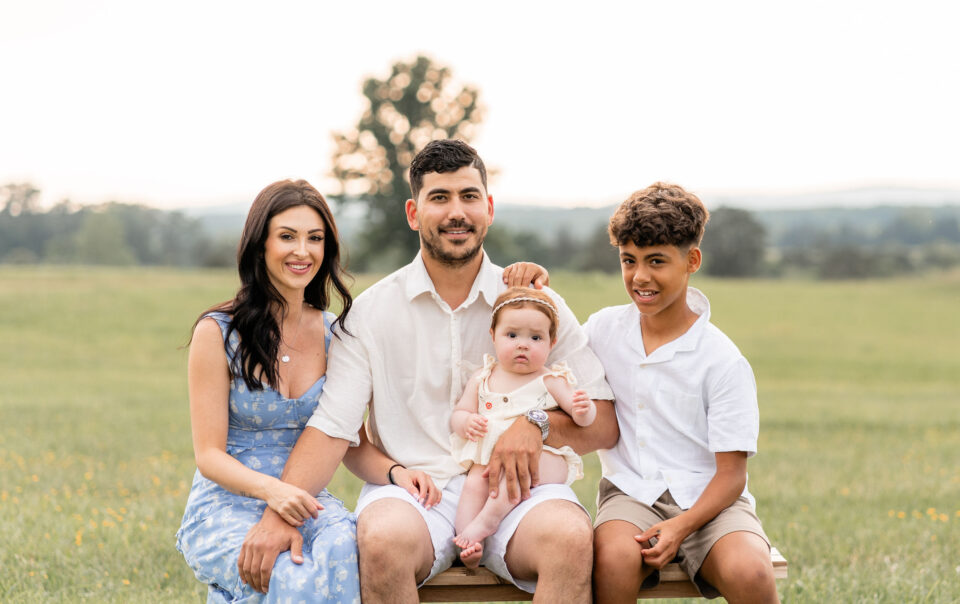 Family of four smiling and posing at Manassas Battlefield Park during sunset.