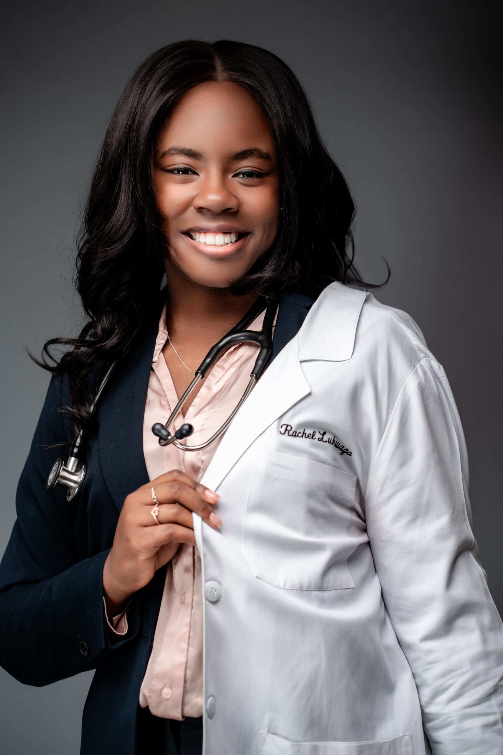 A medical graduate school student wears her white doctor's jacket and poses for a portrait at a studio photo session.